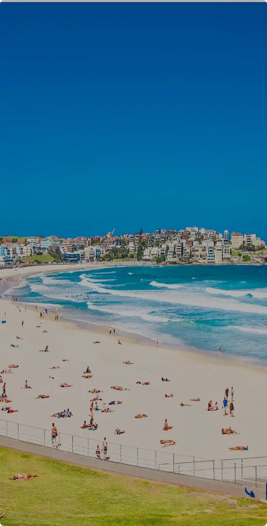 Bondi Beach in Sydney on a sunny day with people relaxing on the sand and colorful buildings along the coast