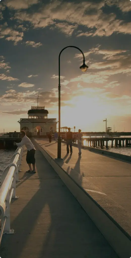 St. Kilda Pier in Melbourne at sunset with people walking along the boardwalk